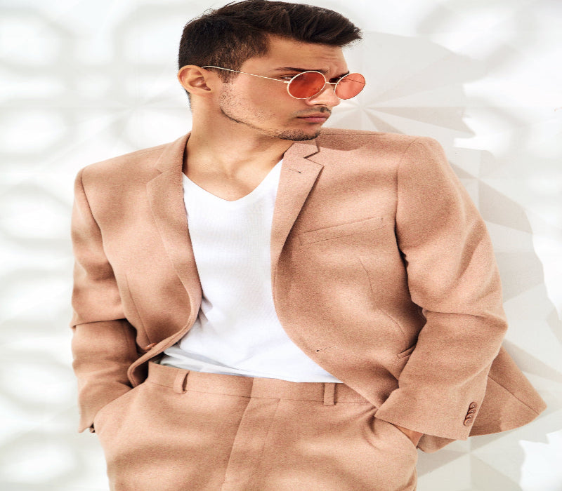 Man wearing a beige suit and sunglasses against a white background